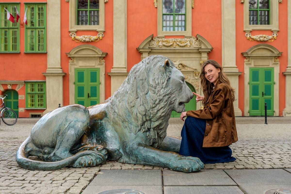 Uśmiechnięta kobieta przy pomniku lwa przy fontannie Czterech Kwartałów w Gdańsku.