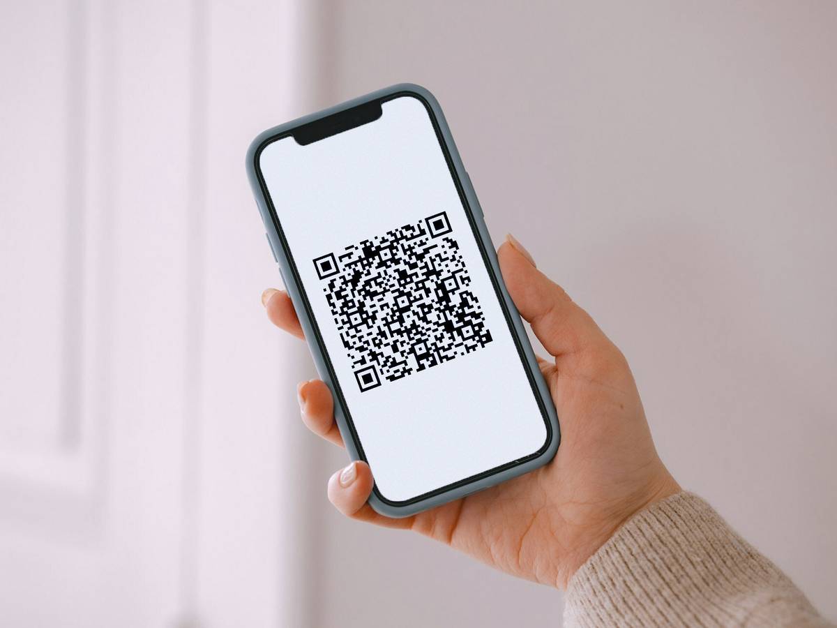 Ręka trzymająca telefon z kodem QR.