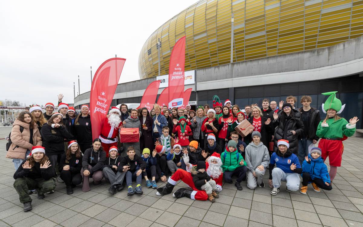 Grupa ludzi w różnym wieku w świątecznych ubraniach, w tle stadion Polsat Plus Arena Gdańsk.